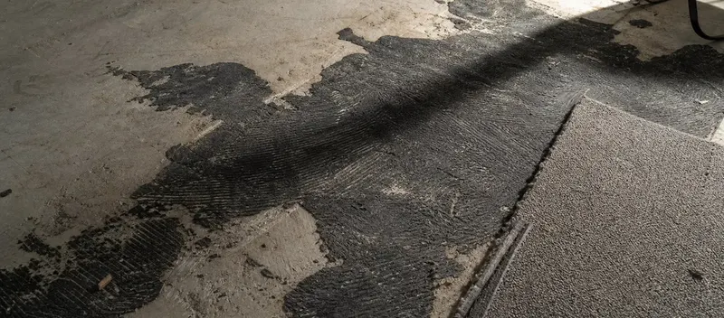 Alter schwarzer Teppichkleber auf Betonboden mit teilweise entferntem Teppichboden in einer Schweizer Altbauwohnung